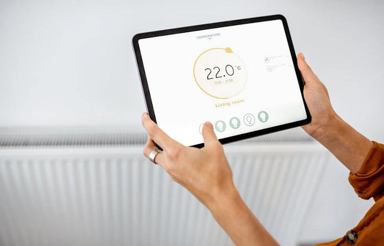 Mains tenant une tablette affichant un thermostat connecté à 22 degrés