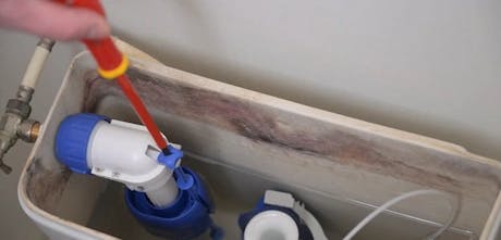 Main avec tournevis réglant le mécanisme d'une chasse d'eau