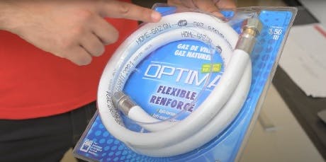 Main tenant un flexible de gaz renforcé Optima dans son emballage