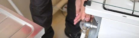 Technicien branchant un flexible de gaz derrière une cuisinière