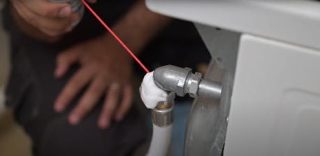 Main désignant un raccord de tuyauterie avec un niveau laser rouge