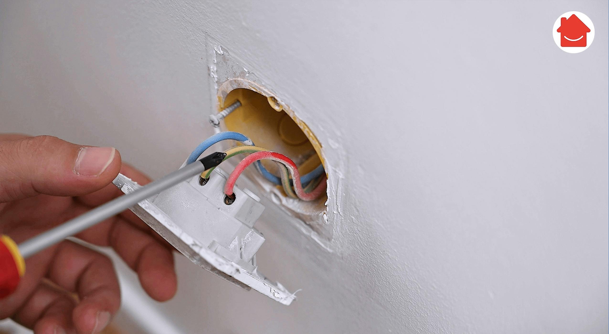 Main vissant des fils électriques colorés dans une prise murale endommagée