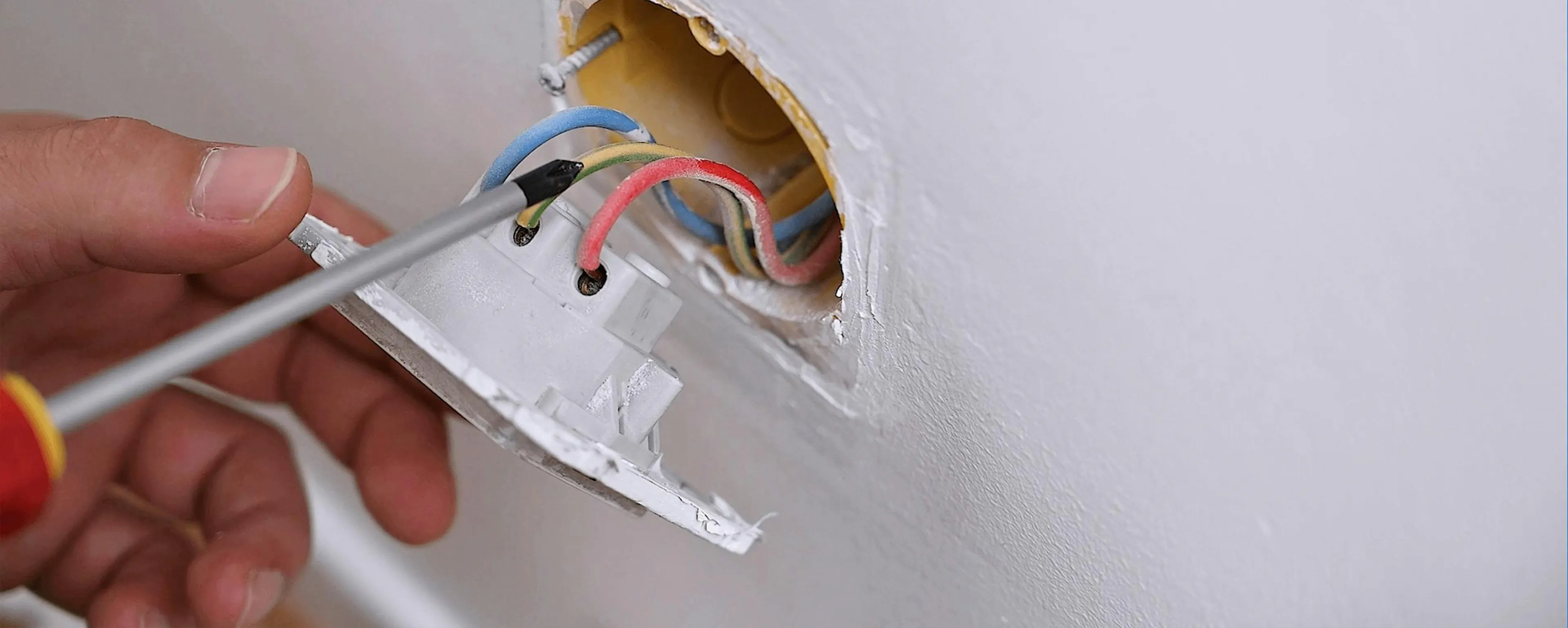 Main vissant des fils électriques dans une prise électrique murale endommagée à changer