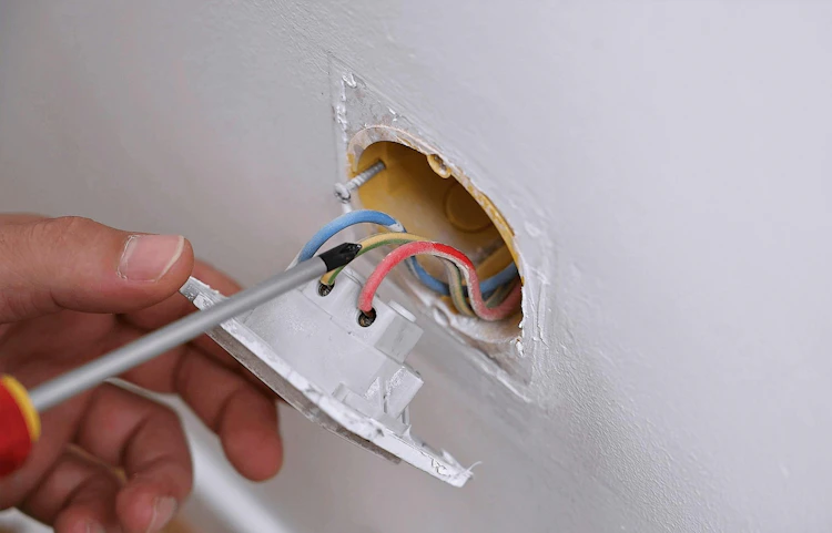 Main vissant des fils électriques colorés dans une prise murale endommagée