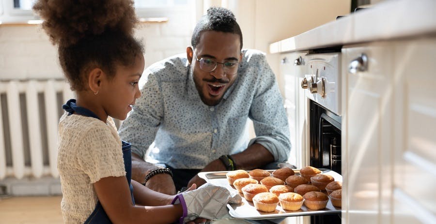 Un père et sa fille sortent une plaque de muffins du four dans leur cuisine
