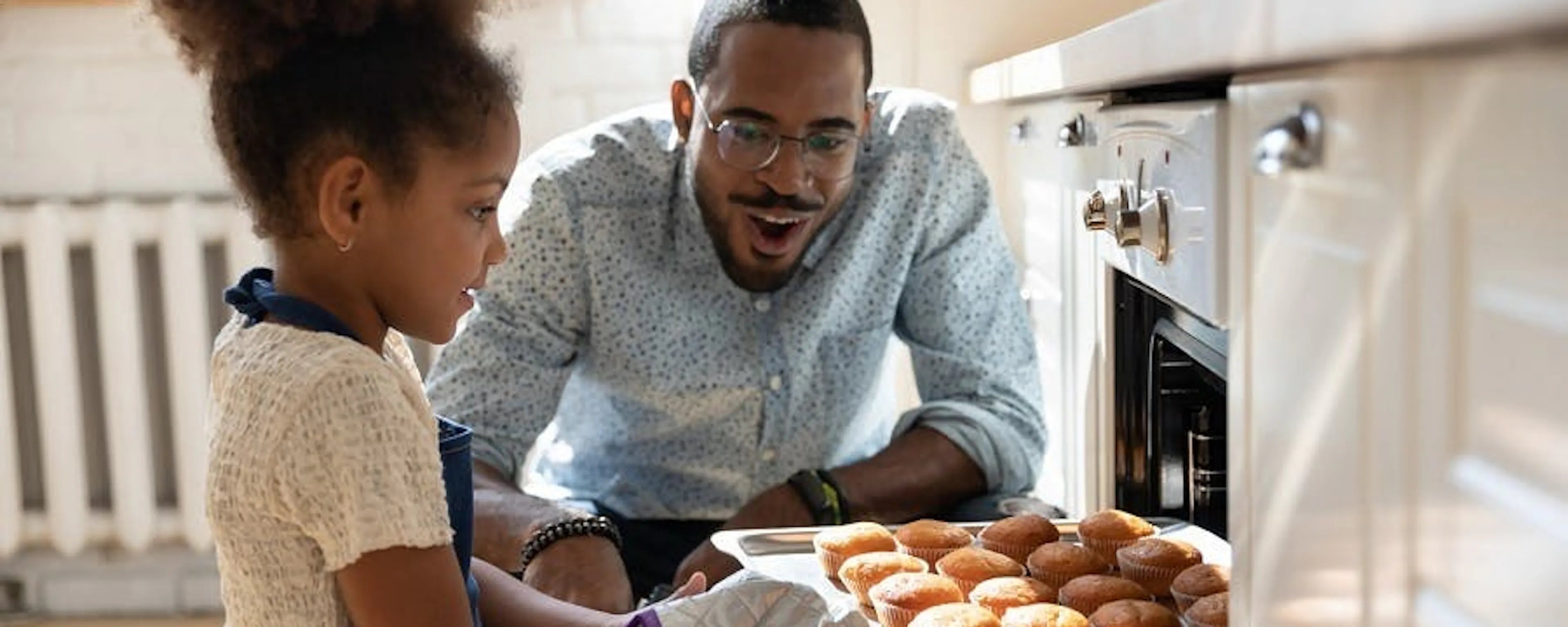 Père et fille sortant une plaque de muffins d'un four en panne dans leur cuisine