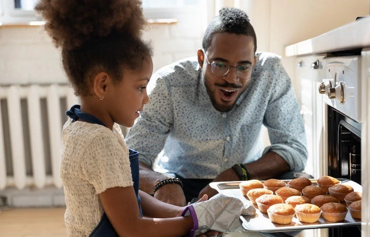 Un père et sa fille sortent une plaque de muffins du four dans leur cuisine