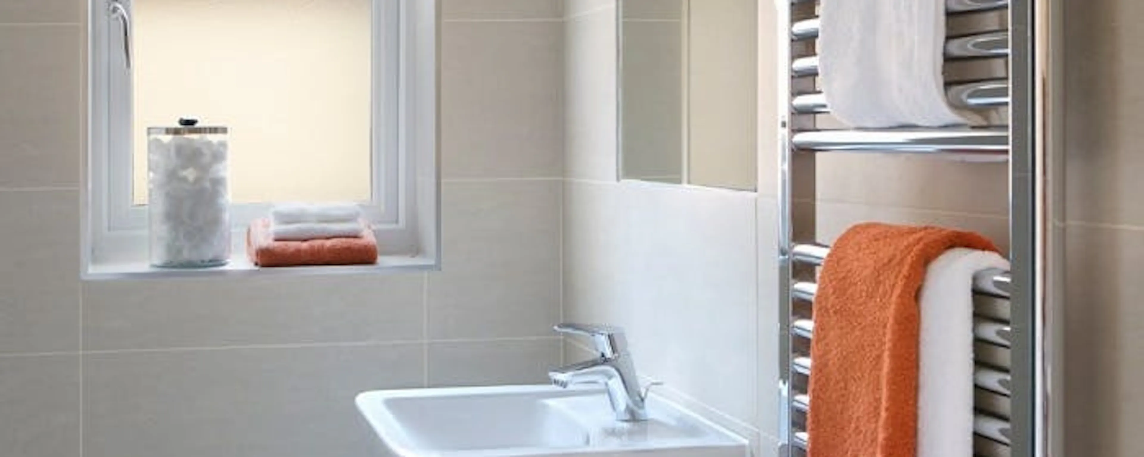 Sèche-serviette chromé en panne et à réparer, avec serviettes blanches et orange dans une salle de bain