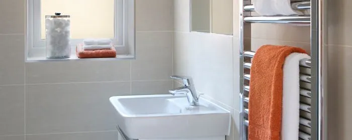 Sèche-serviette chromé en panne et à réparer, avec serviettes blanches et orange dans une salle de bain