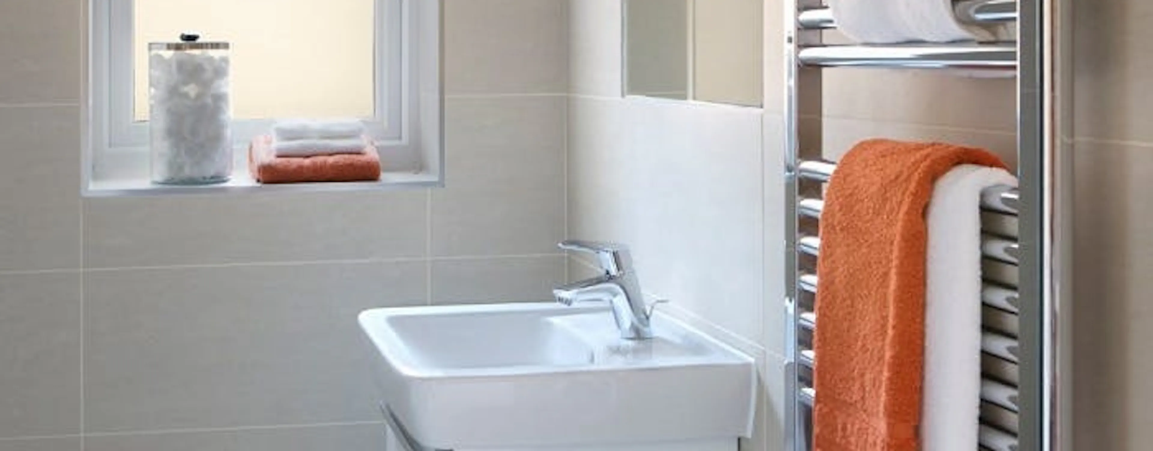 Sèche-serviette chromé en panne et à réparer, avec serviettes blanches et orange dans une salle de bain