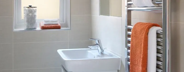 Sèche-serviette chromé en panne et à réparer, avec serviettes blanches et orange dans une salle de bain