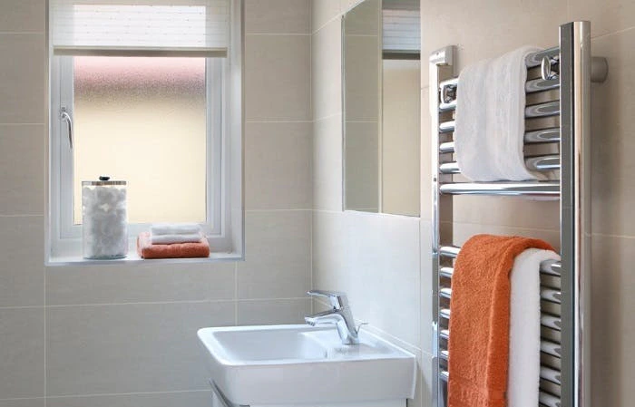 Sèche-serviette chromé avec serviettes blanches et orange dans une salle de bain moderne