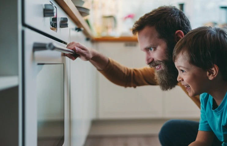 Père et enfant regardant l'intérieur d'un four de cuisine