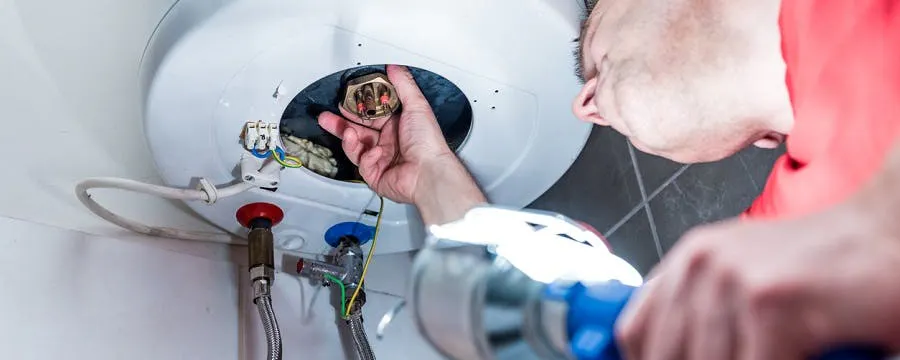Technicien vérifiant les raccordements d'un ballon d'eau chaude qui fuit, avec une clé