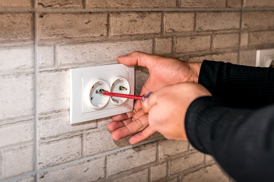 Mains tenant un tournevis près d'une prise électrique murale