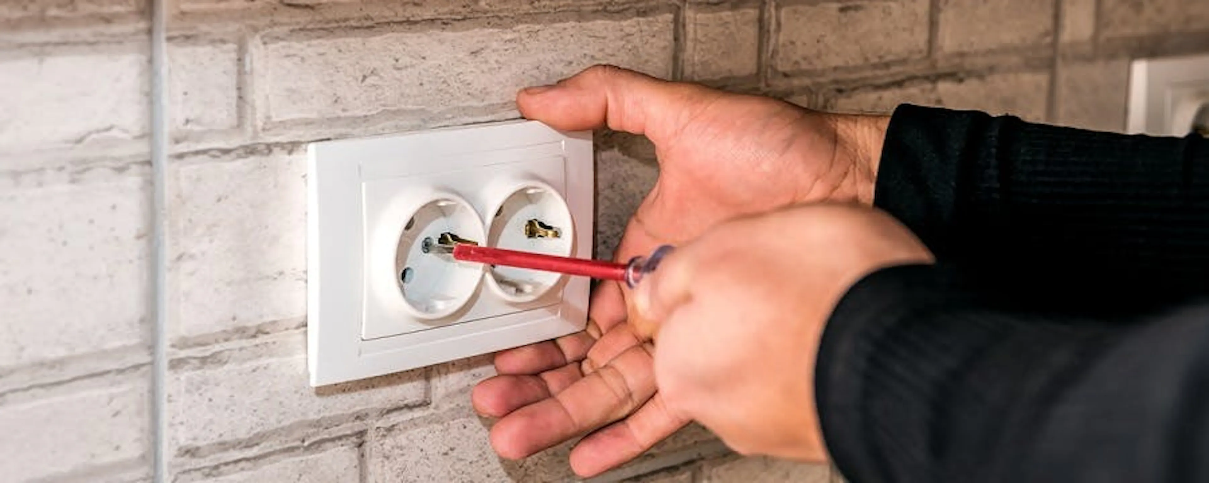 Mains avec tournevis en train de réparer une prise de courant murale qui fait du bruit