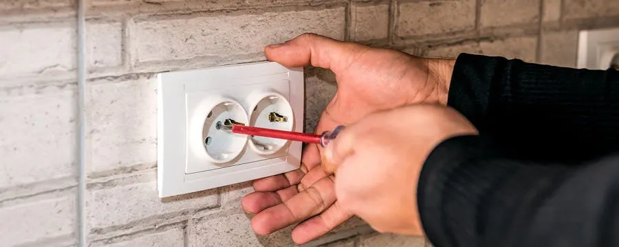 Mains avec tournevis en train de réparer une prise de courant murale qui fait du bruit