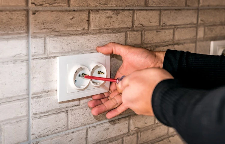 Mains tenant un tournevis près d'une prise électrique murale