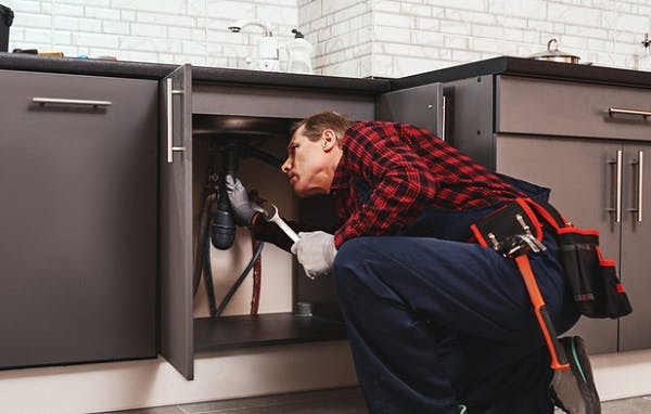 Plombier réparant des tuyaux sous un évier de cuisine
