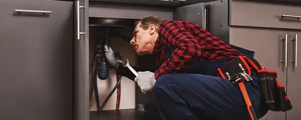 Plombier réparant un siphon sous un évier de cuisine