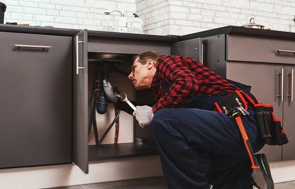 Plombier réparant des tuyaux sous un évier de cuisine