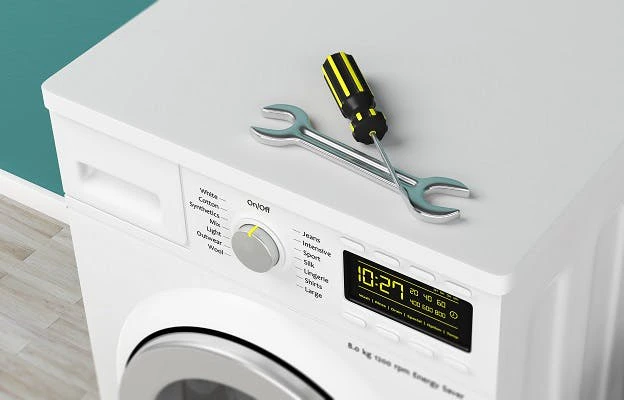 Machine à laver avec clé et tournevis posés dessus