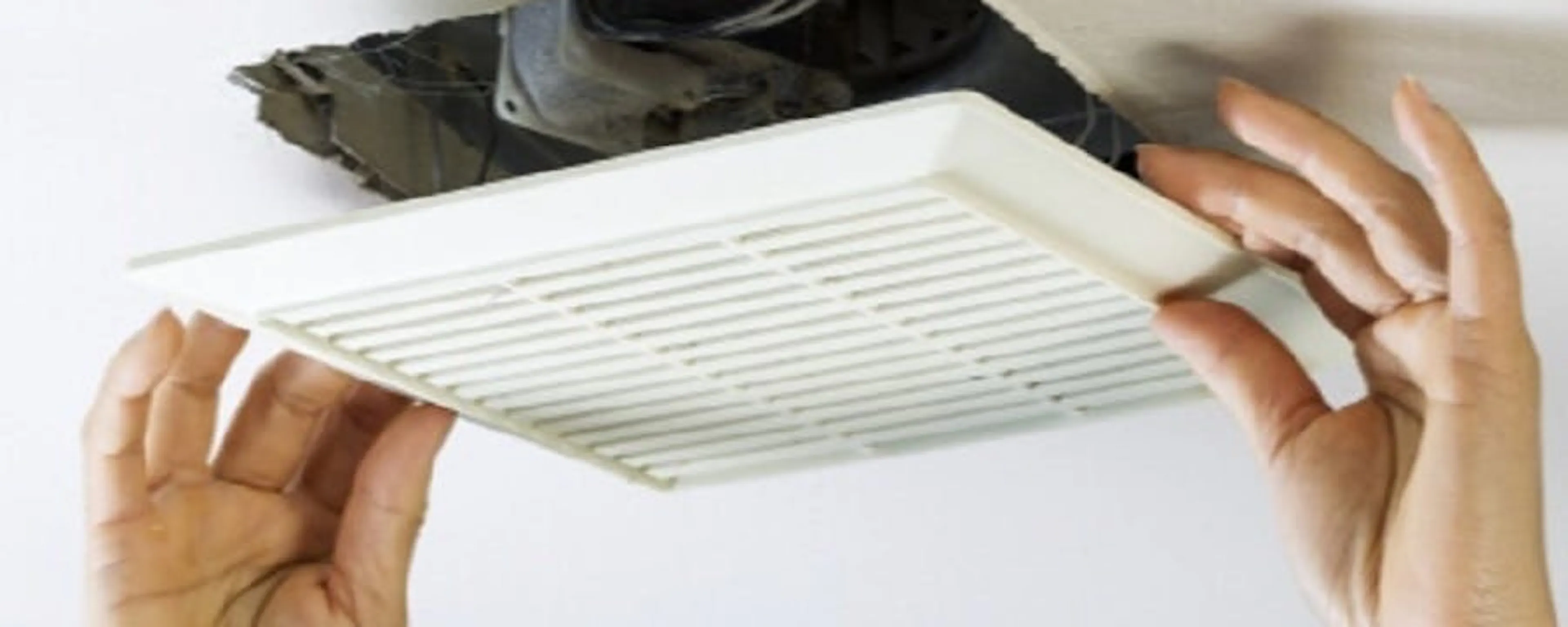 Mains installant une grille de ventilation au plafond dans une maison