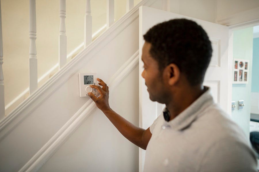 Homme réglant un thermostat mural blanc dans un couloir