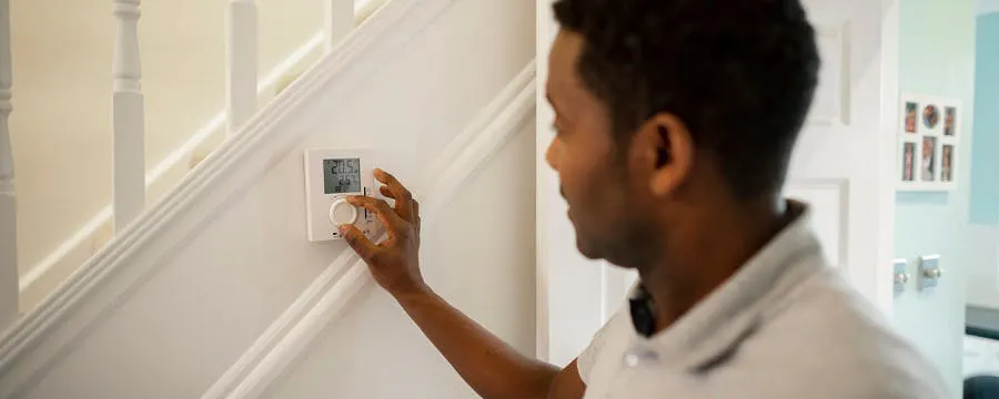 Homme réglant un thermostat mural afin de chauffer son intérieur à la température idéale