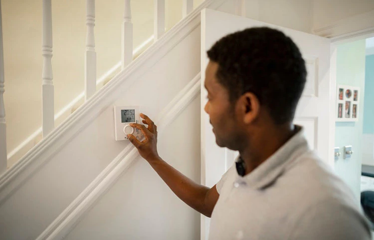 Homme réglant un thermostat mural blanc dans un couloir