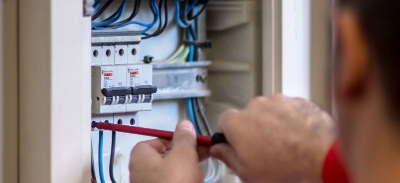 Technicien intervenant sur un tableau électrique avec des disjoncteurs et des câbles