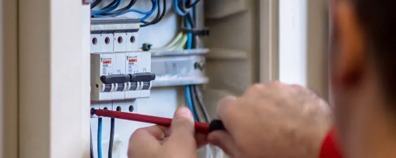 Technicien vérifiant et changeant un fusible électrique sur un tableau avec disjoncteurs et câbles