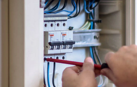 Technicien intervenant sur un tableau électrique avec des disjoncteurs et des câbles