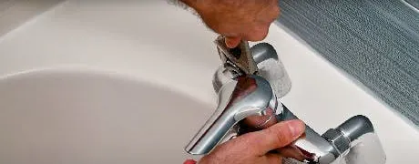 Mains réparant un robinet de lavabo chromé