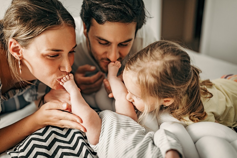 Parents et fillette embrassant tendrement un nouveau-né sur un lit