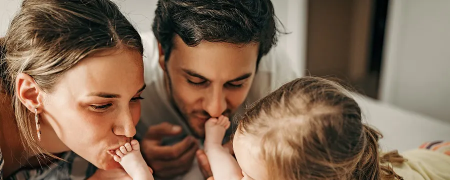 Parents et fillette embrassant tendrement un nouveau-né sur un lit