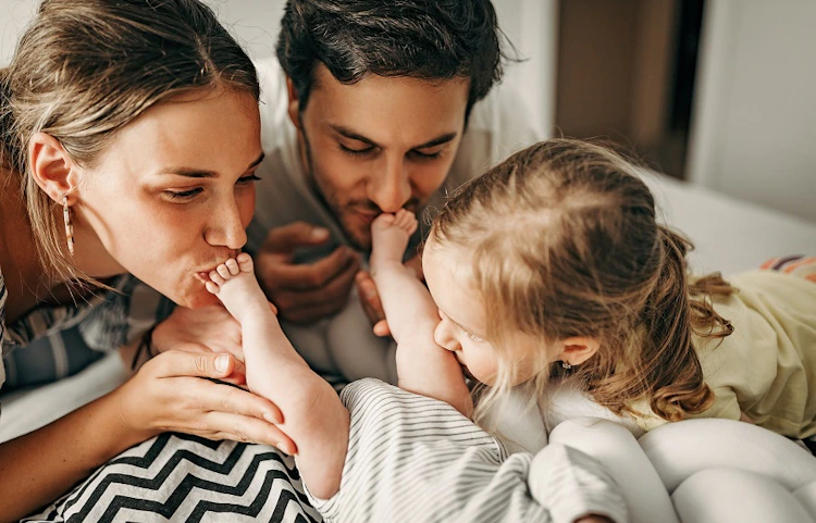 Parents et fillette embrassant tendrement un nouveau-né sur un lit