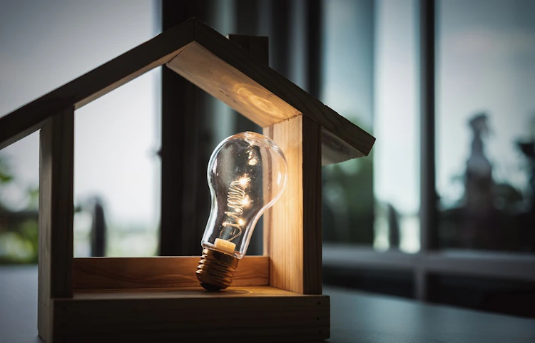 Ampoule dans une maquette de maison en bois éclairée sur bureau