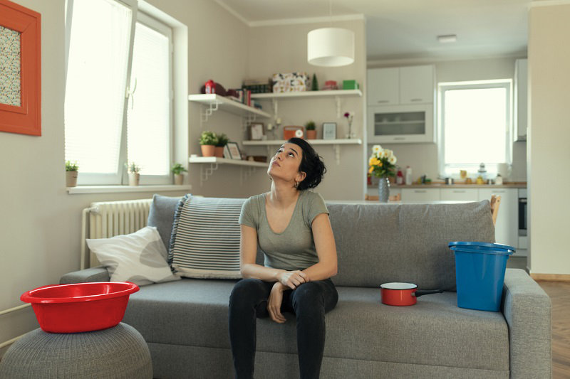 Femme assise sur un canapé avec des seaux recueillant des fuites d'eau