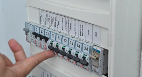 Doigt pointant un disjoncteur dans un tableau électrique numéroté