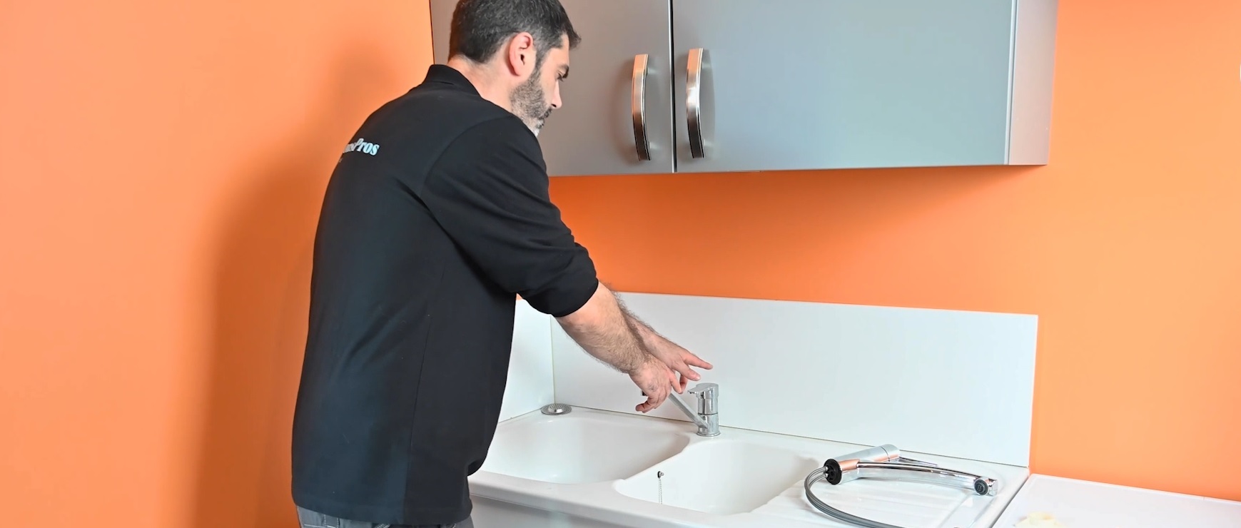 Technicien en noir installant un robinet sur plan de travail orange