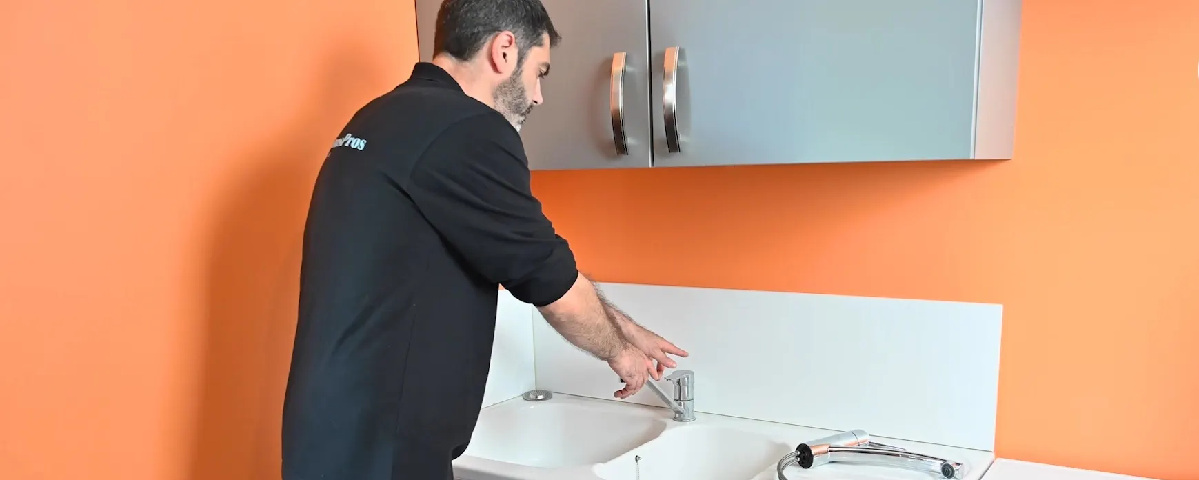 Technicien en noir installant un robinet sur plan de travail orange