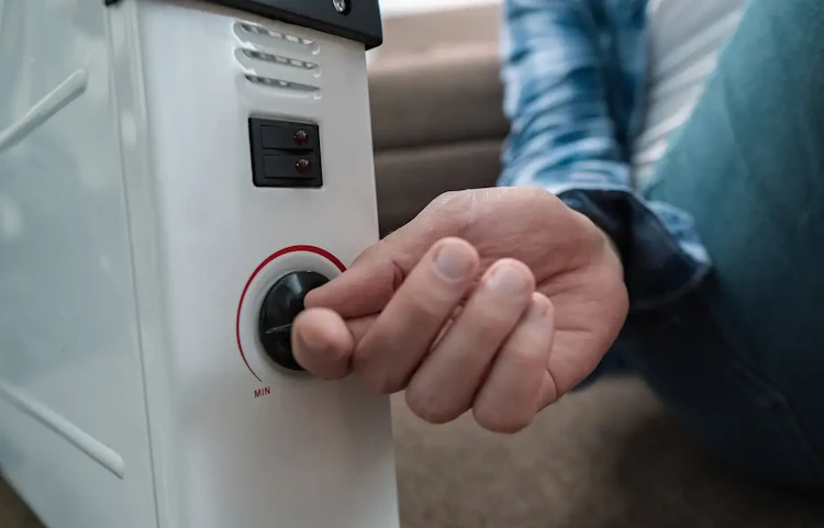 Main réglant le thermostat d'un radiateur à bain d'huile blanc