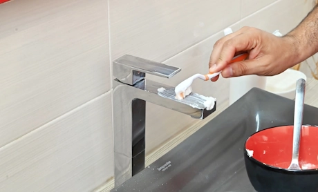 Main nettoyant un robinet chromé avec une brosse à dents