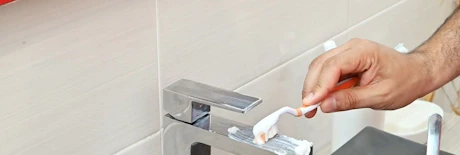 Main nettoyant un robinet chromé avec une brosse à dents