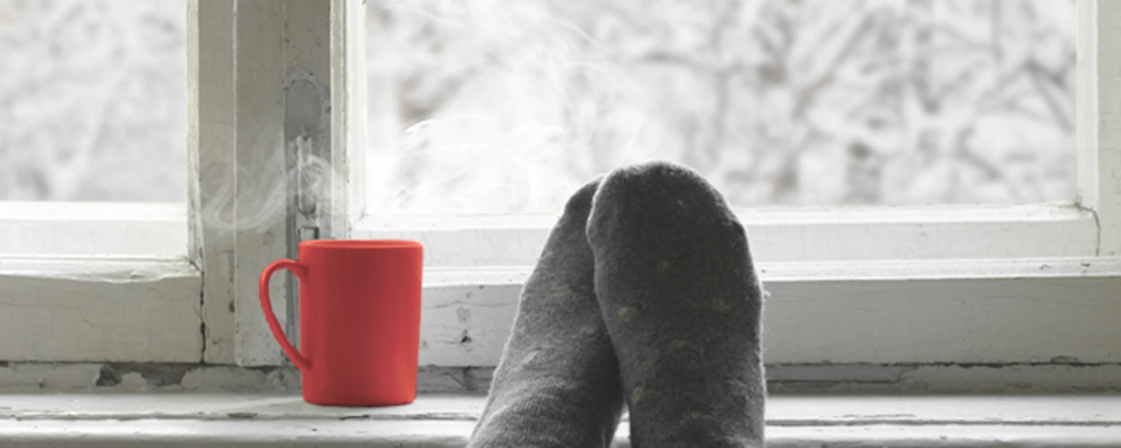 Pieds chaussés de chaussettes grises posés sur un radiateur devant fenêtre enneigée