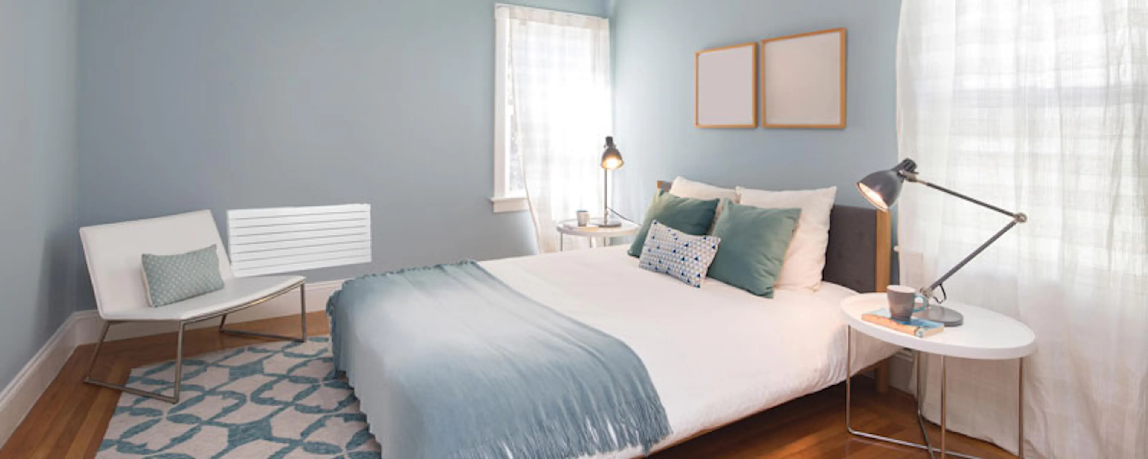 Chambre lumineuse aux murs bleus avec grand lit blanc et parquet