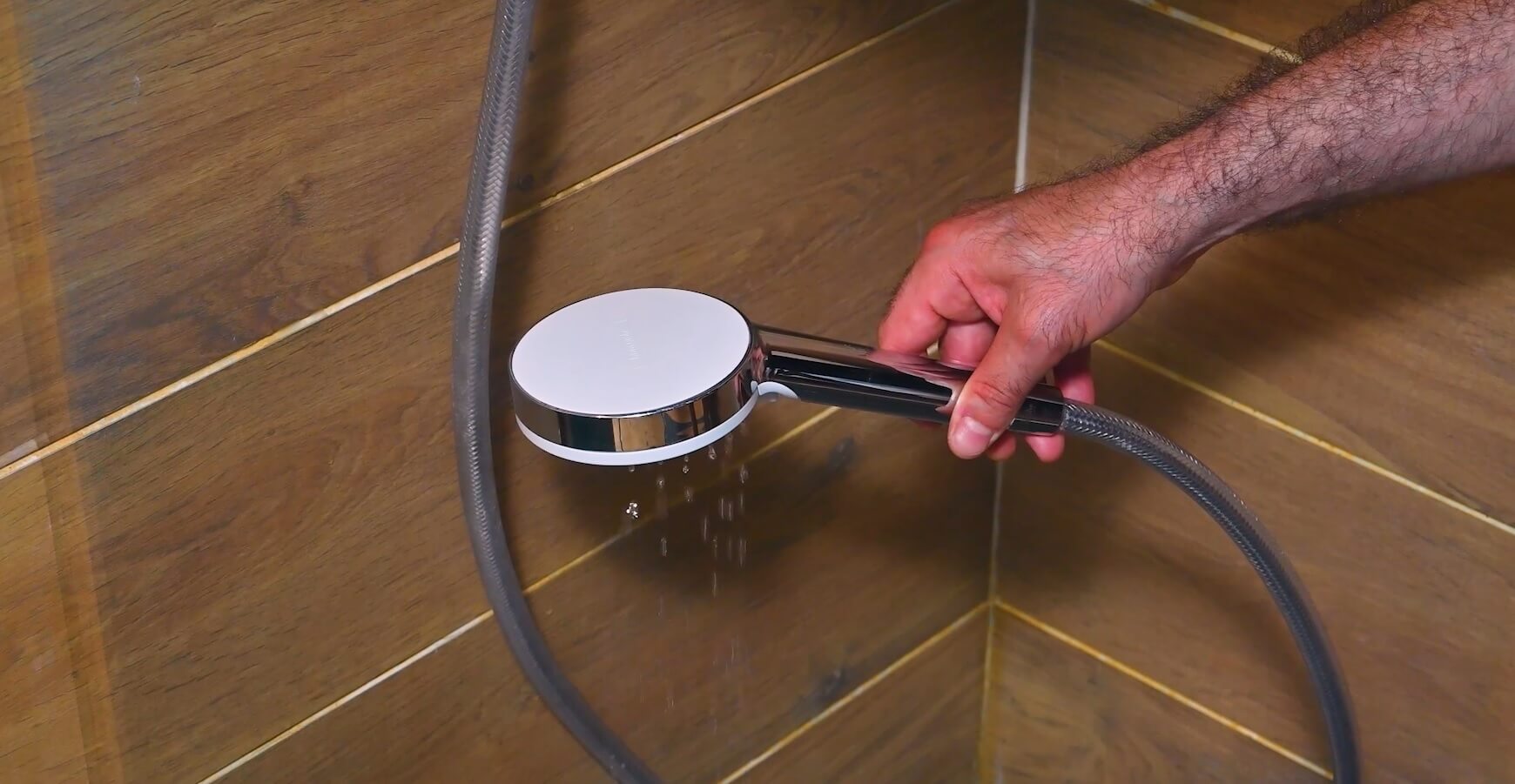 Main tenant un pommeau de douche chromé au-dessus d'un sol carrelé