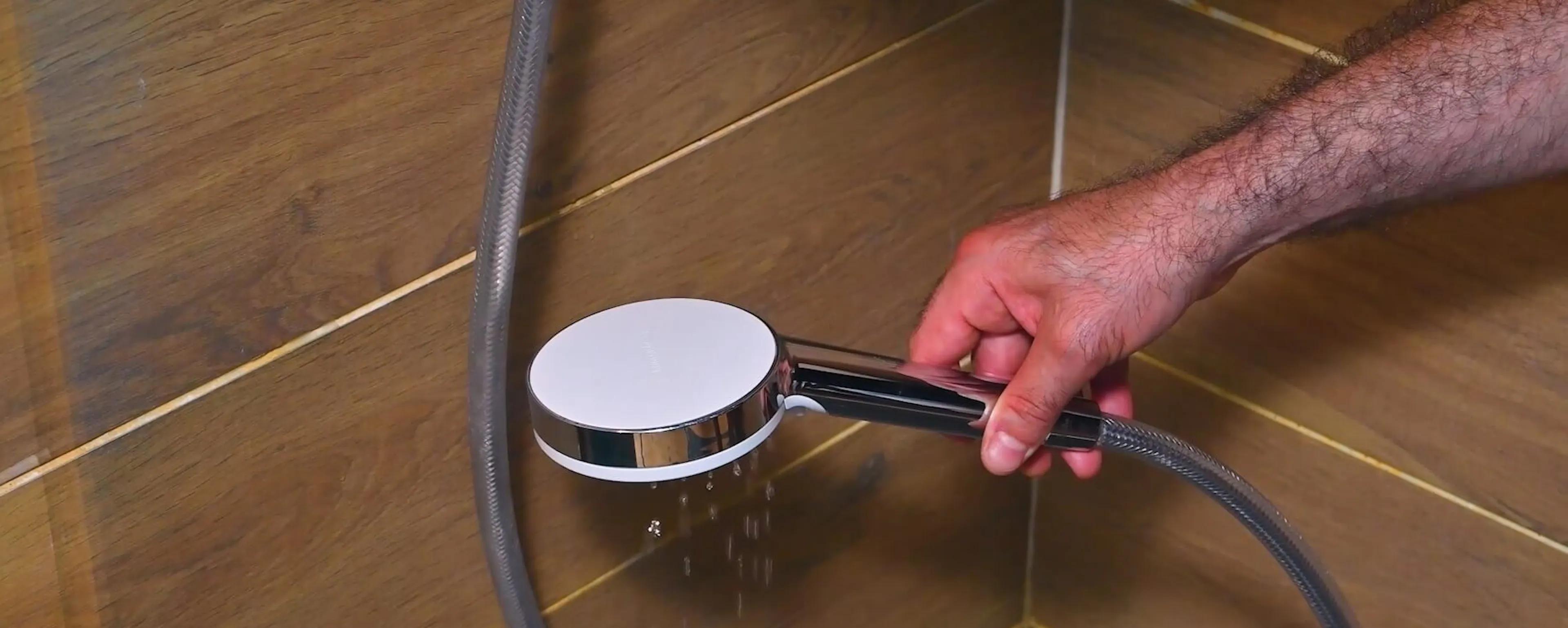 Main tenant un pommeau de douche chromé au-dessus d'un sol carrelé