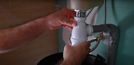 Mains manipulant les raccords de tuyauterie sous un lavabo